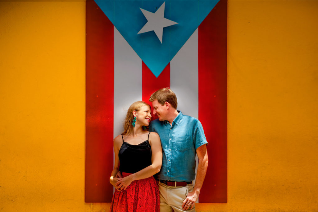 A couple poses in front of a Puerto Rican flag during their Old San Juan engagement session